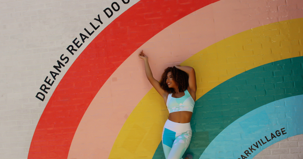 woman feeling expressive in her My Velveteen Habit Yoga clothes under a rainbow painted on a wall